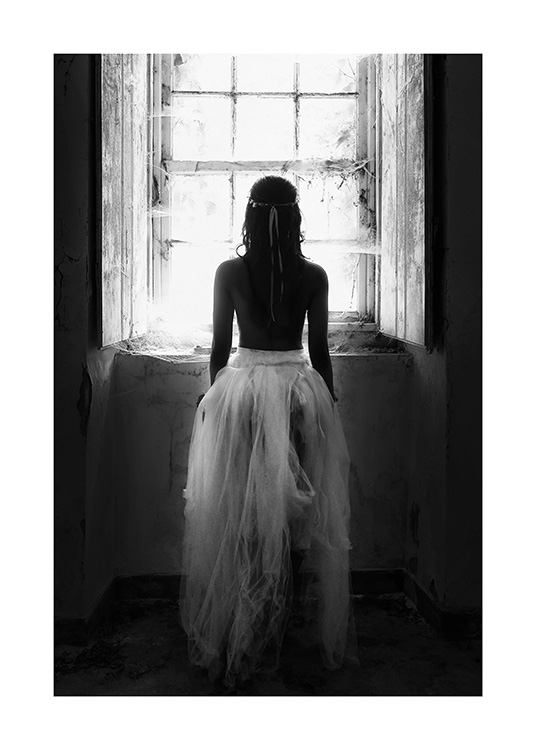Black and white photograph of woman standing in front of window in tulle skirt