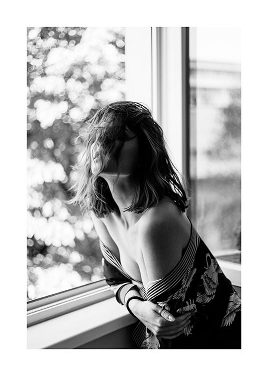 Black and white photograph of woman leaning on window sill in an off shoulder top