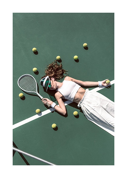  – Photograph of a girl in white trousers and a white top laying on a tennis court surrounded by tennis balls
