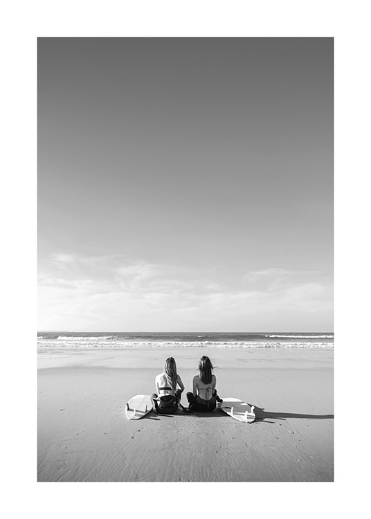 – Black and white photograph of two girls sitting next to each other on the beach with their surfboards