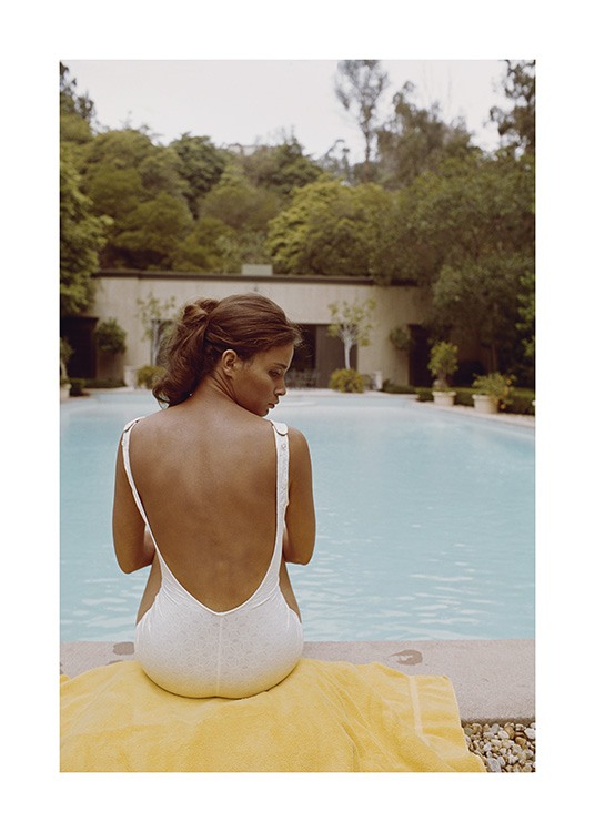  – Photograph of a woman sitting on a towel in front of a pool, wearing a white swimsuit