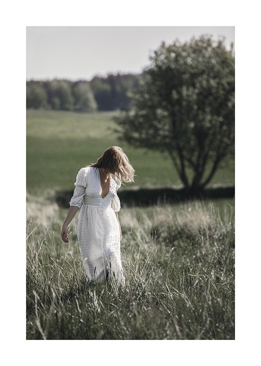  – Photograph of a woman wearing a white dress, standing in a grass field with trees in the background