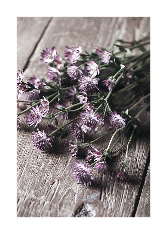  – Photograph of small, purple flowers with green leaves in a bundle, laying on a wooden table
