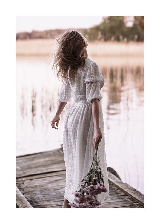  – Photograph of a woman standing on a small pier, wearing a white dress and holding a bouquet of flowers