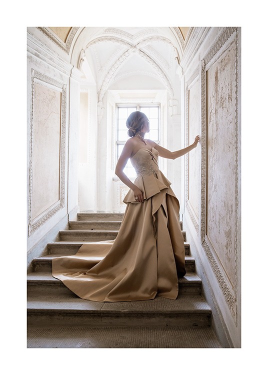  – Photograph of a woman in a gold and beige dress, standing in a staircase in a baroque style