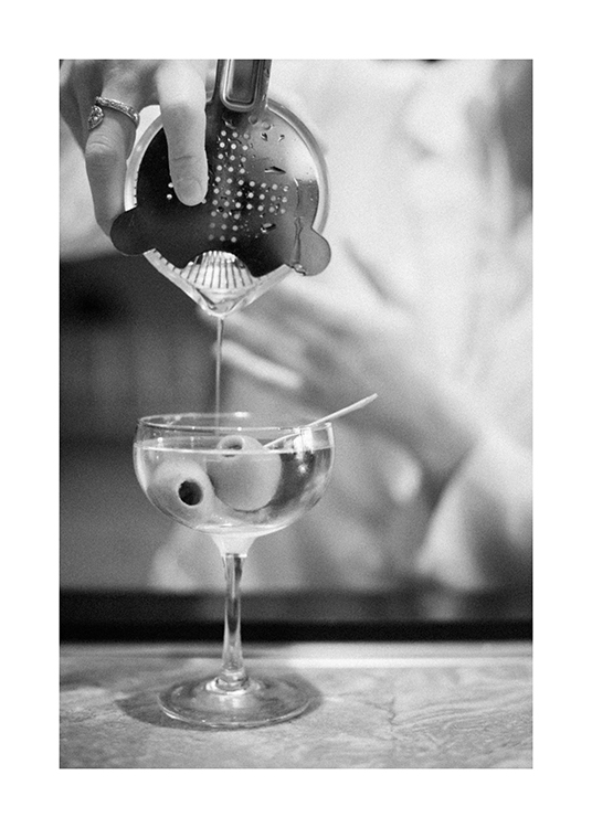  – Black and white photograph of a martini being poured from a drink shaker, with olives in the glass