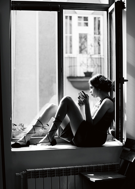  – Black and white photograph of a woman sitting in an open window, holding a cup