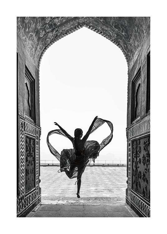 – Black and white photograph of a woman dancing on one leg in a flowy dress, framed by an arch