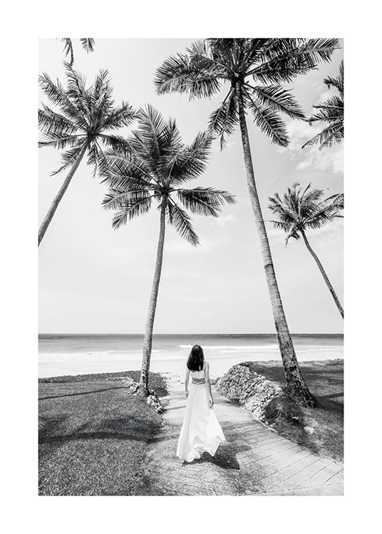  – Black and white photograph of a woman standing between palm trees in a long dress