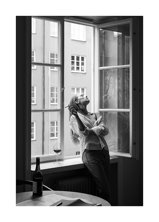  – Black and white photograph of a woman holding a cigarette, leaning back in an open window