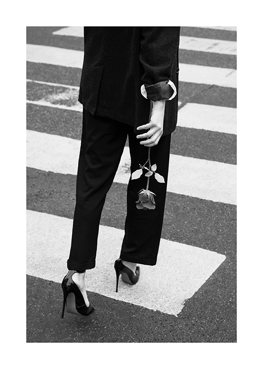  – Black and white photograph of a woman walking on a pedestrian crossing in a suit and heels, holding a rose