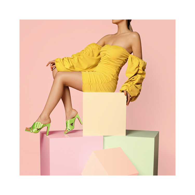  – A woman sitting on the top of coloured boxes in a yellow dress and green heels