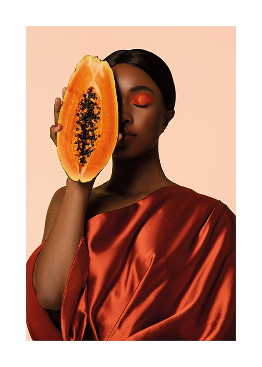  – A woman in a satin dress holding a sliced papaya up to her face