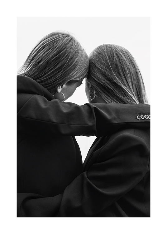  – Black and white photograph of a pair of women in suits leaning their heads against each other