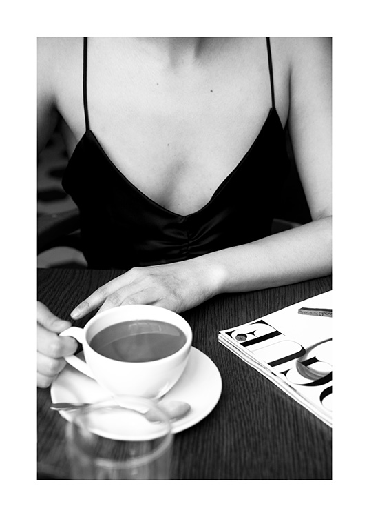  – Black and white photograph of a woman sitting at a café with a coffee cup on the table