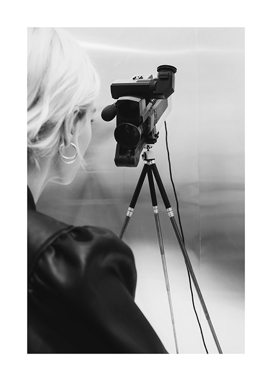  – Black and white photograph of a woman with blond hair standing behind a video camera