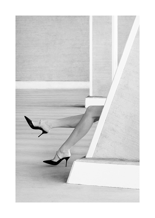 – Black and white photograph of a pair of legs with high heels on, sticking out from behind a wall