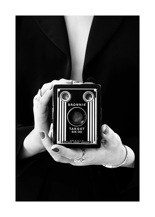 – Black and white photograph of a woman holding a vintage camera in front of her body