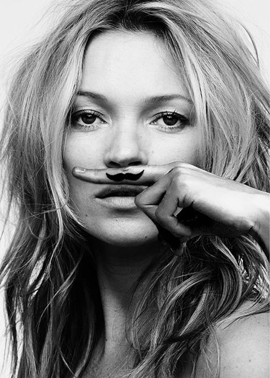  – Black and white photograph of Kate Moss with a finger above her mouth with a moustache on the finger