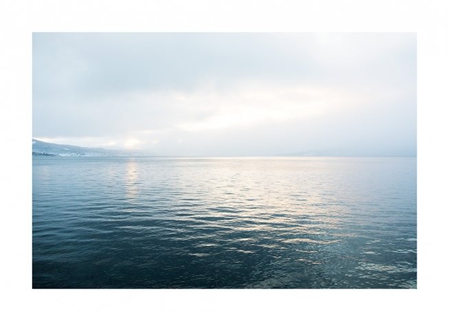  - Photograph of an ocean in sunlight with still water and mountains in the background